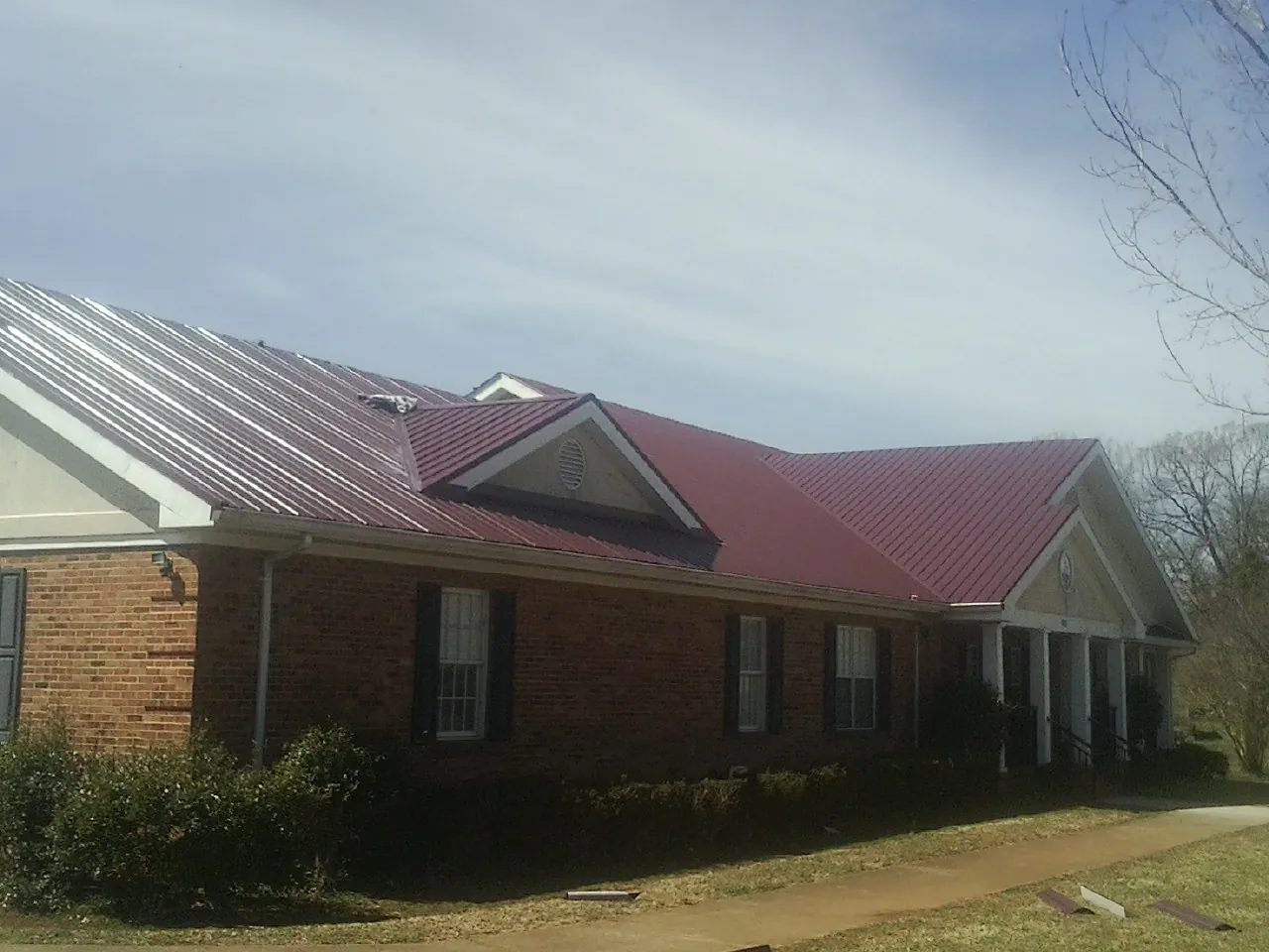 Red metal roof with gabled entries on a long brick building, from a Hail Damage Roof Repair job in Creston