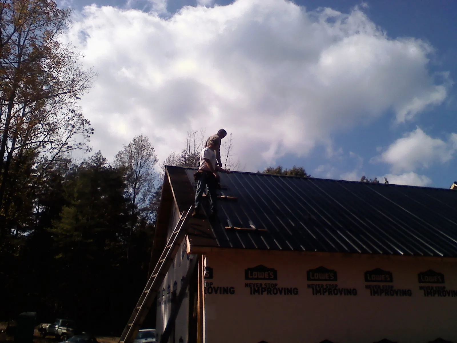 Roofer fastening dark metal panels high against a cloudy sky, from a Roof Inspection job in Creston